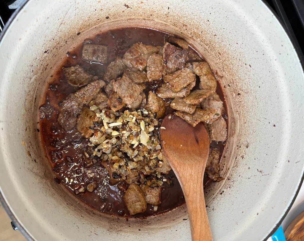 Enameled cast iron pot with reduced red wine, seared beef strips, caramelized onions, garlic and herbs.