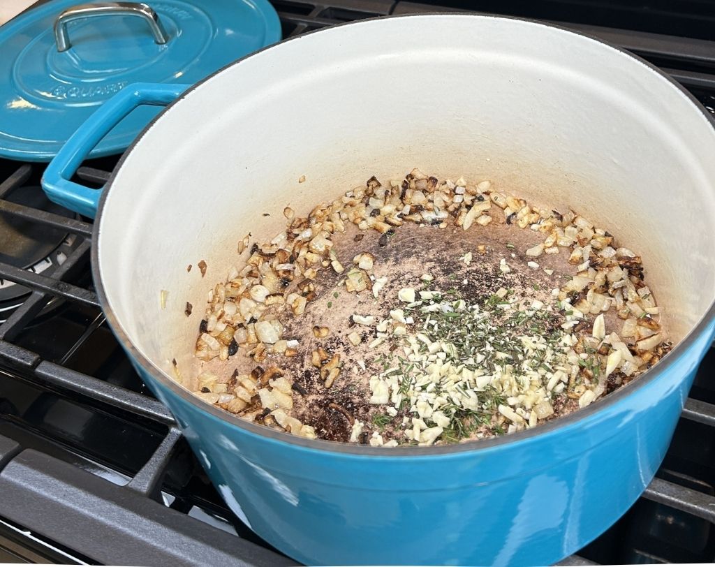 Enameled cast iron pot with caramelized onions, fresh herbs and chopped garlic.