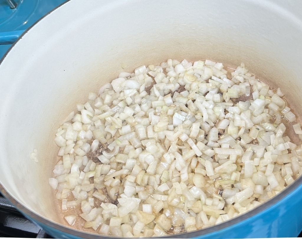 Enameled cast iron pot with bits chopped onions cooking.