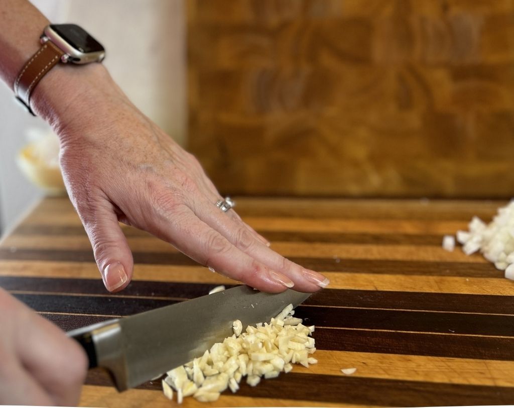 Wooden cutting board with woman's hands chopping garlic.