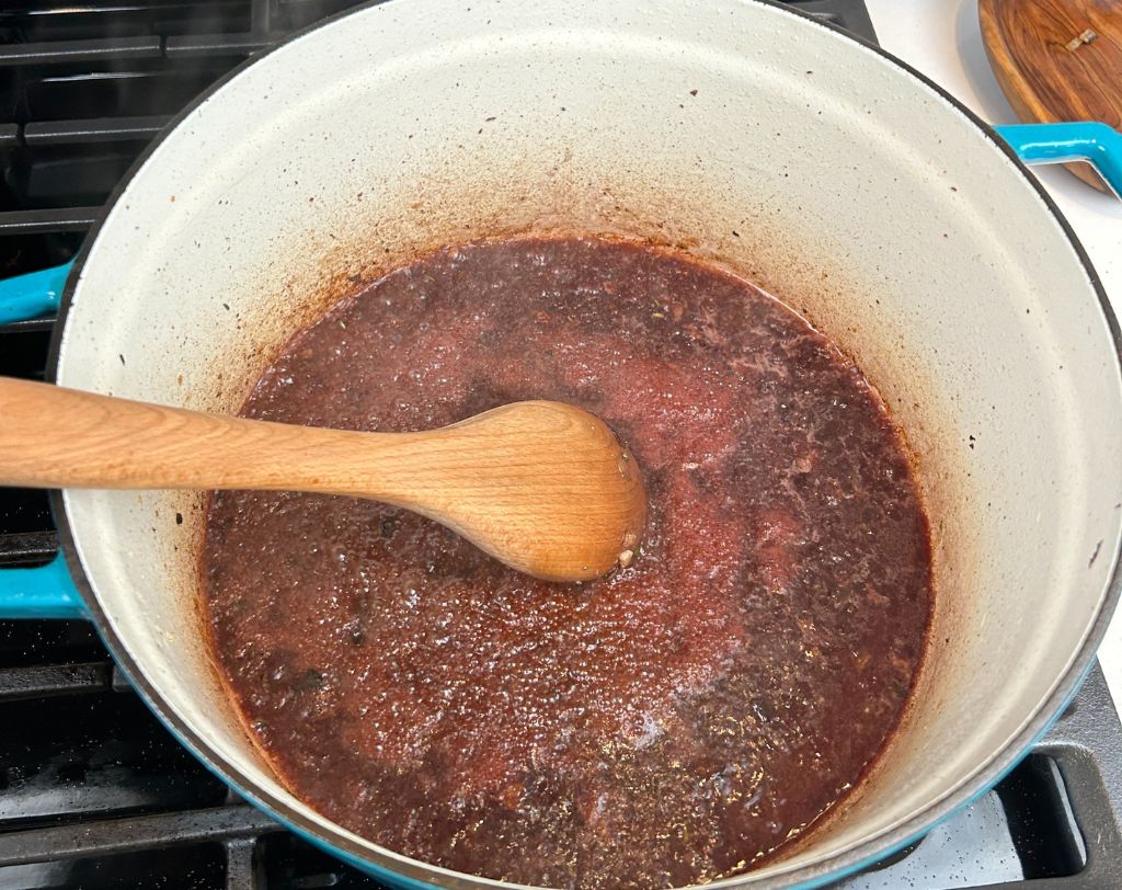 Enameled cast iron pot with red wine wooden spoon and red wine mixture reducing.