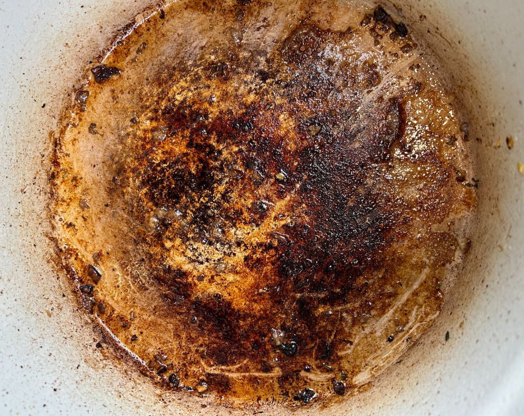 Enameled cast iron pot with bits of golden brown fond in bottom.