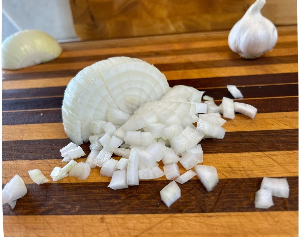 Yellow peeled onion on wood cutting board with radial cuts and chopped onions.