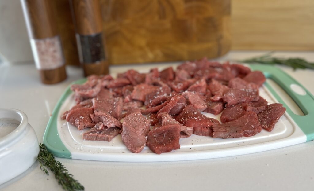 White and aqua cutting board with sliced beef seasoned with salt and pepper.