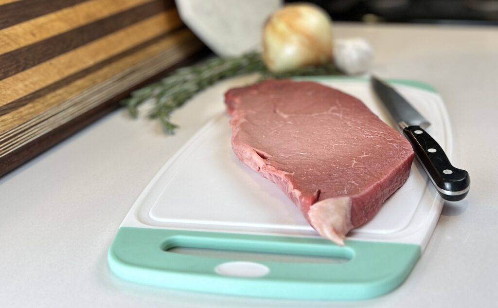 White and aqua cutting board with London broil , utility knife.