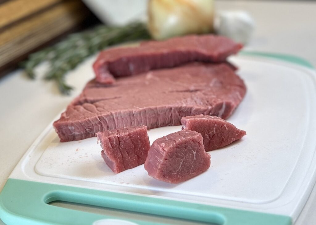 White and aqua cutting board with London broil cubed and sliced