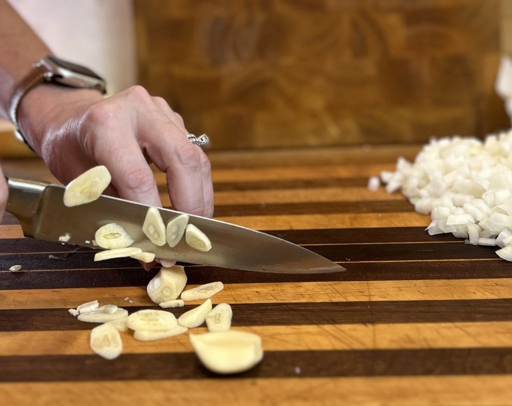 Woman's hands slicing garlic clove with utility knife.