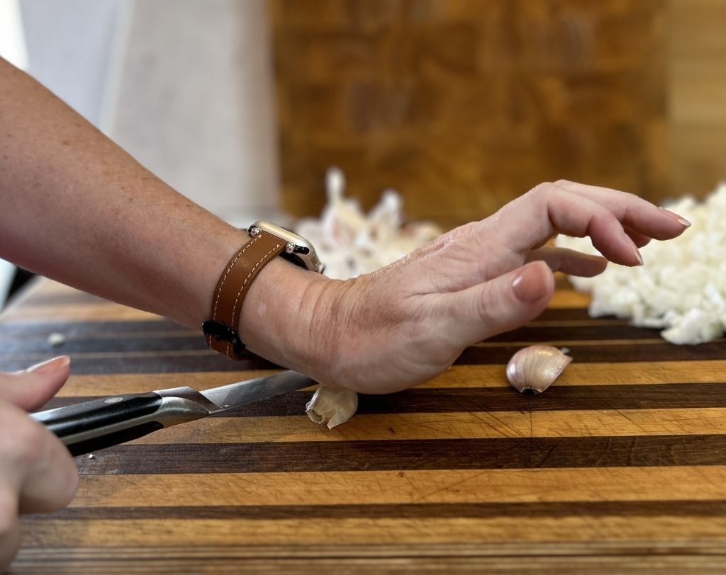 Woman's hands pressing on utility knife to crush clove of garlic.