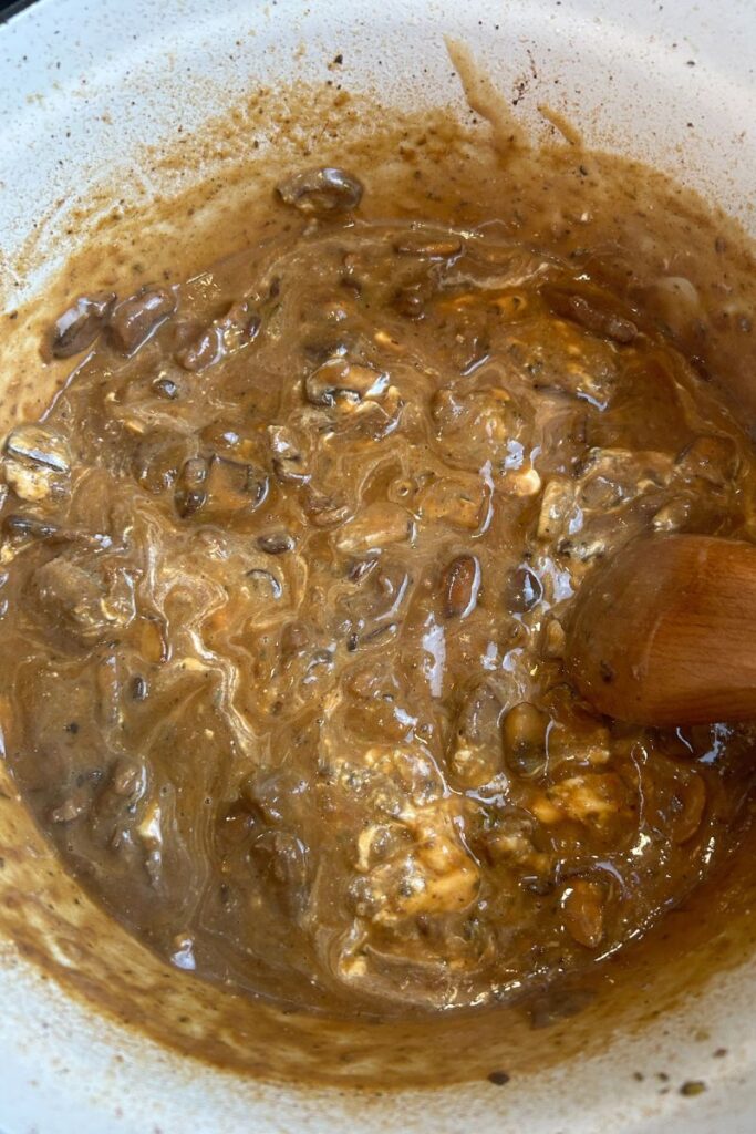 Delicious Beef Stroganoff in enameled cast iron pot with wooden spoon mixing in sour cream.