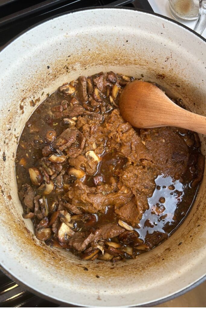 Delicious Beef Stroganoff in enameled cast iron pot with roux being mixed in.