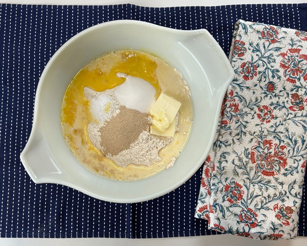 Ingredients in mixing bowl before mixing. Flour, Egg, Yeast, Milk, Butter, Water, Salt and Sugar.