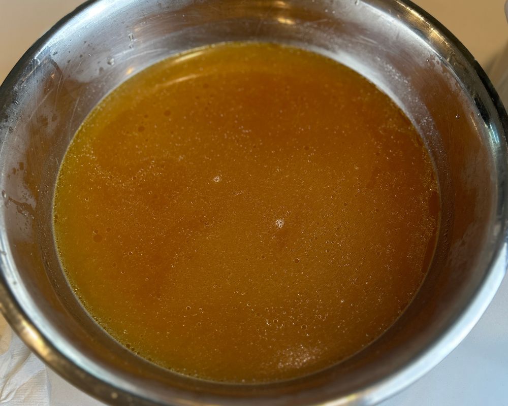 Strained homemade chicken stock in large silver bowl. 