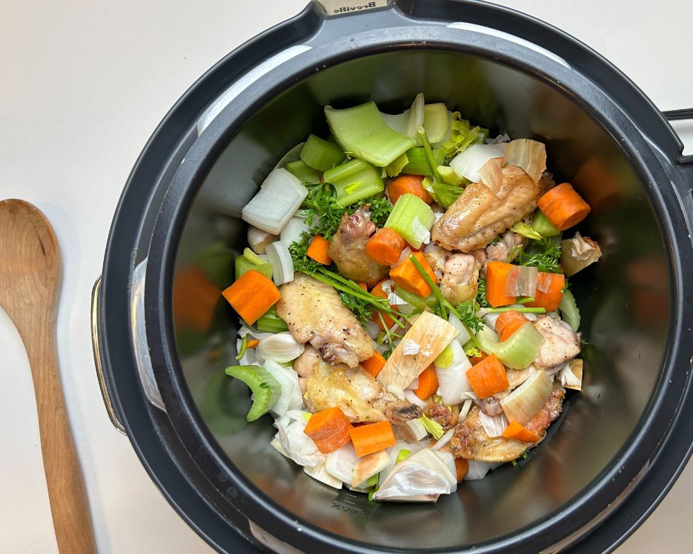 Pressure cooker pot with Homemade Chicken Stock ingredients. Roasted chicken wings, carrots, celery, onion, garlic and parsley.