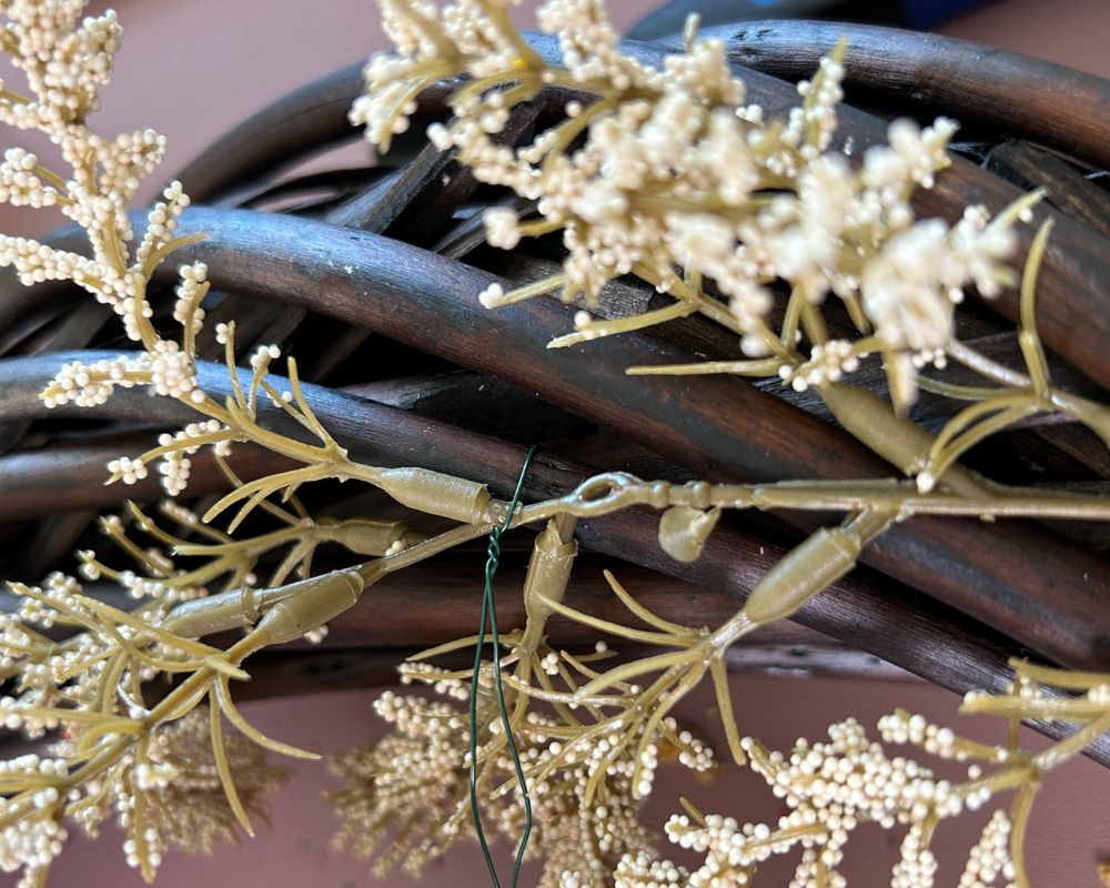 Cream floral pick being attached with green wire to vine wreath