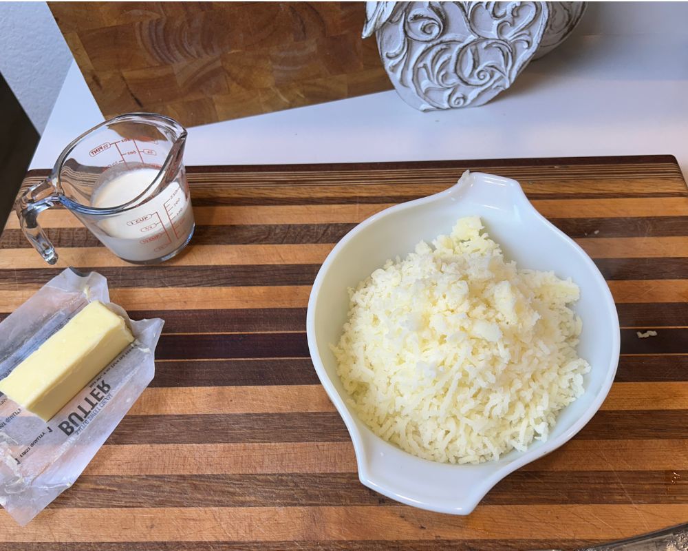 Riced potatoes in serving bowl on stripped cutting board. 