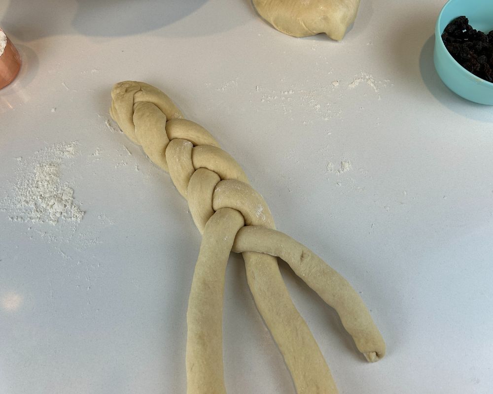 Homemade Challah dough braid half way complete on white counter top.