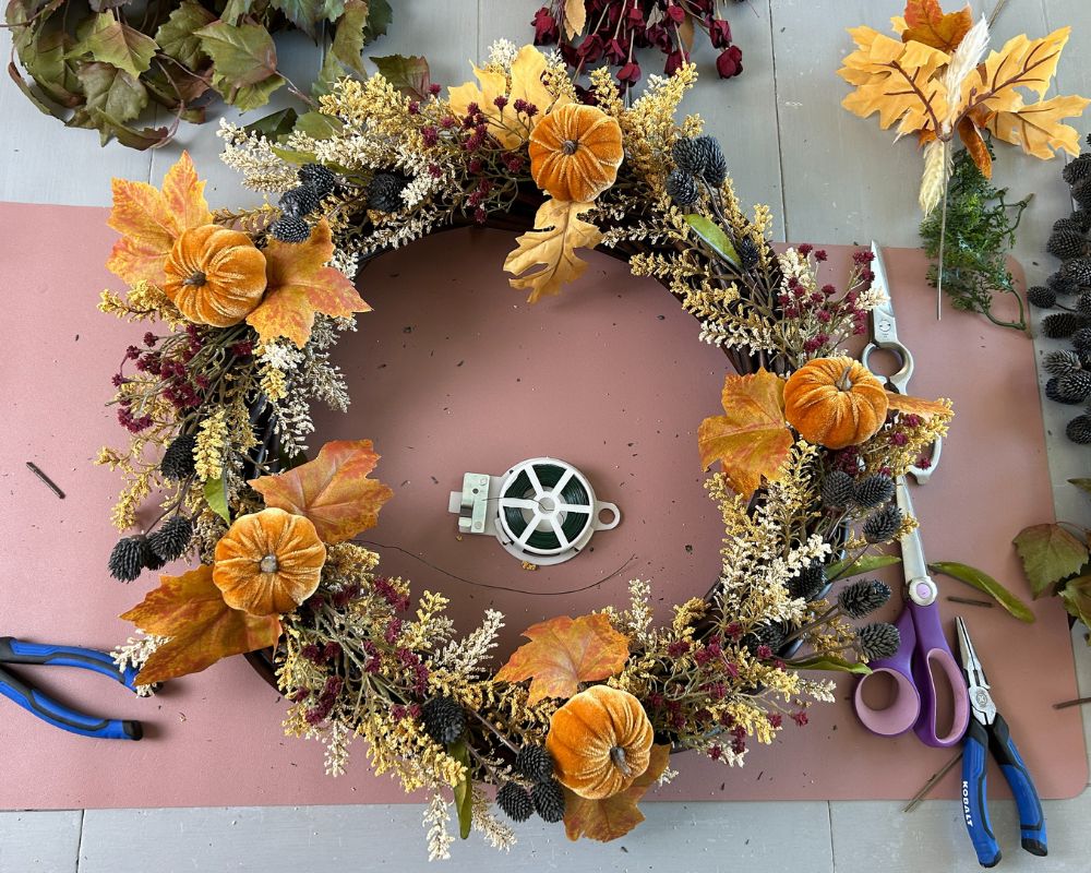 Vine wreath with a mix of floral picks in orange, cream, yellow, burgundy, green and blue.