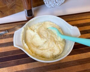 Striped cutting board with dish of mashed potatoes.