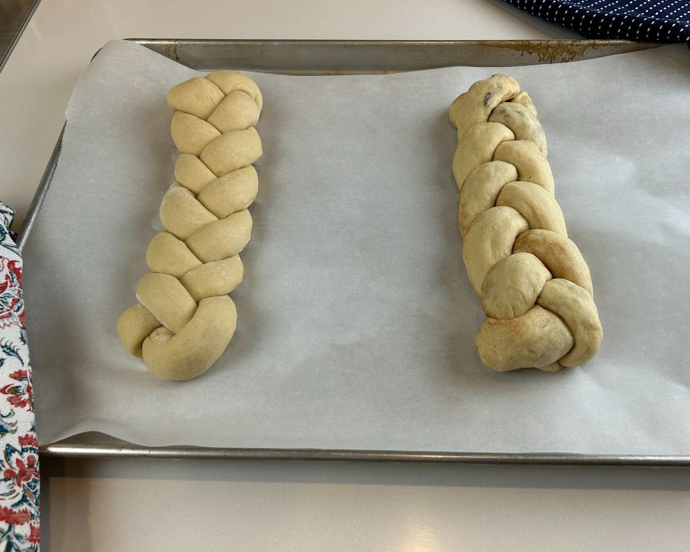 Two Homemade Challah braids on a parchment lined baking sheet.