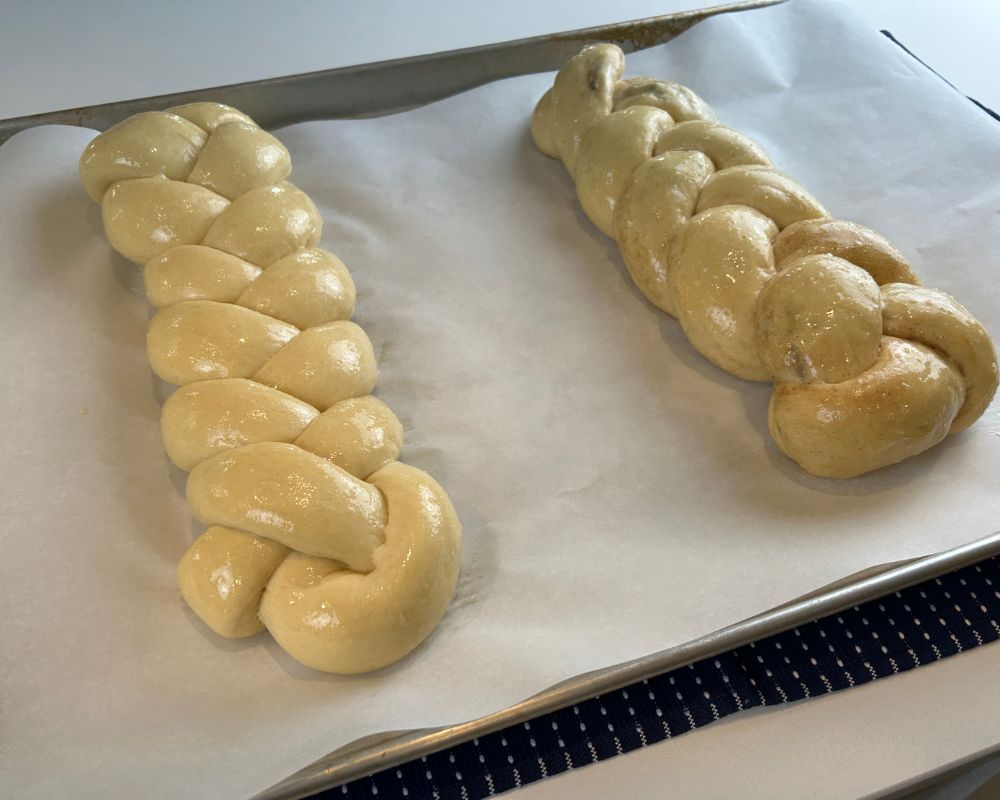 Homemade Challah braids brushed in egg wash on a parchment lined baking sheet. 