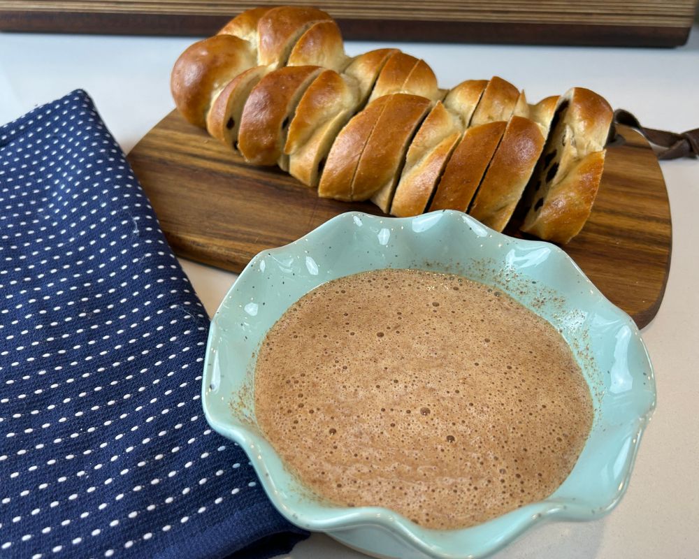 French Toast custard in a light aqua scalloped edge bowl with sliced Challah in the background.