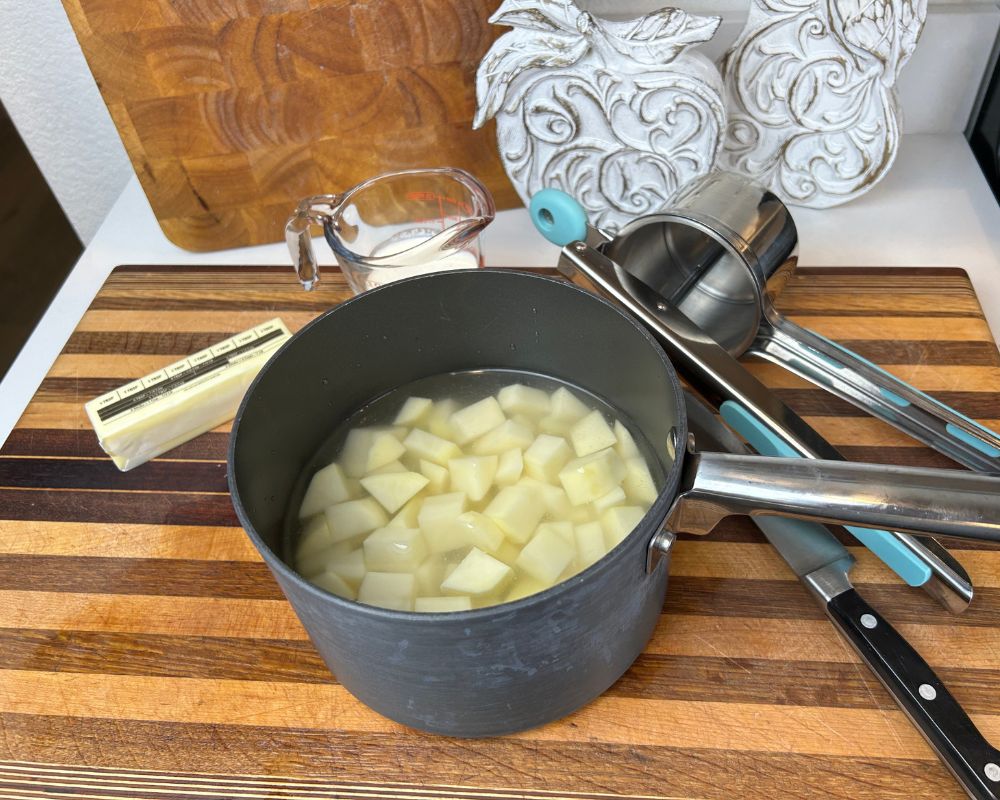 Ingredients on cutting board, including diced potatoes in a pot with water, butter and heavy cream.