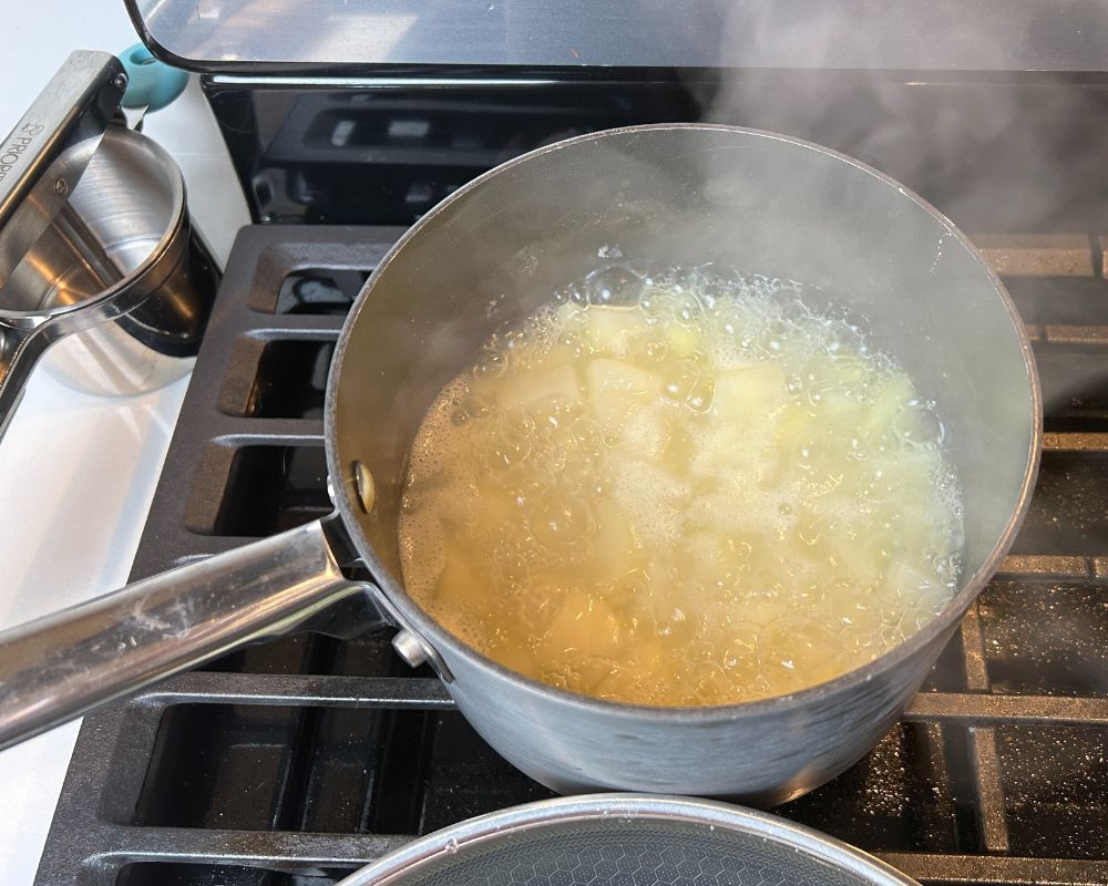 Diced potatoes in a pot of boiling water sitting on a stove top. 