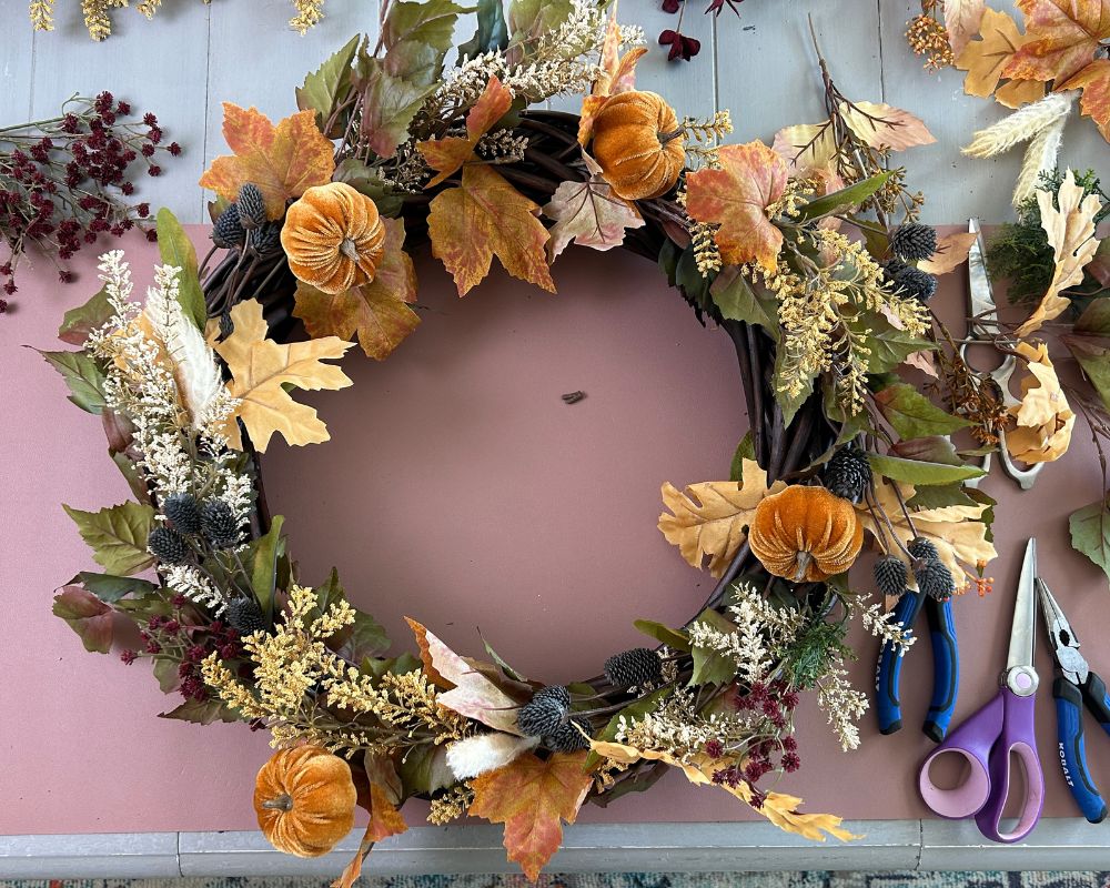 Vine wreath with a mix of floral picks in orange, cream, yellow, burgundy, green and blue.