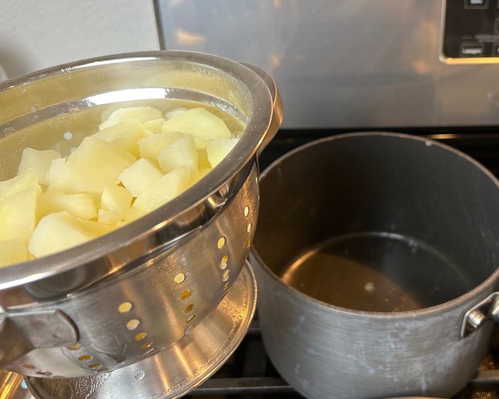 Stove top with empty pot and a small metal colander with drained potatoes. 