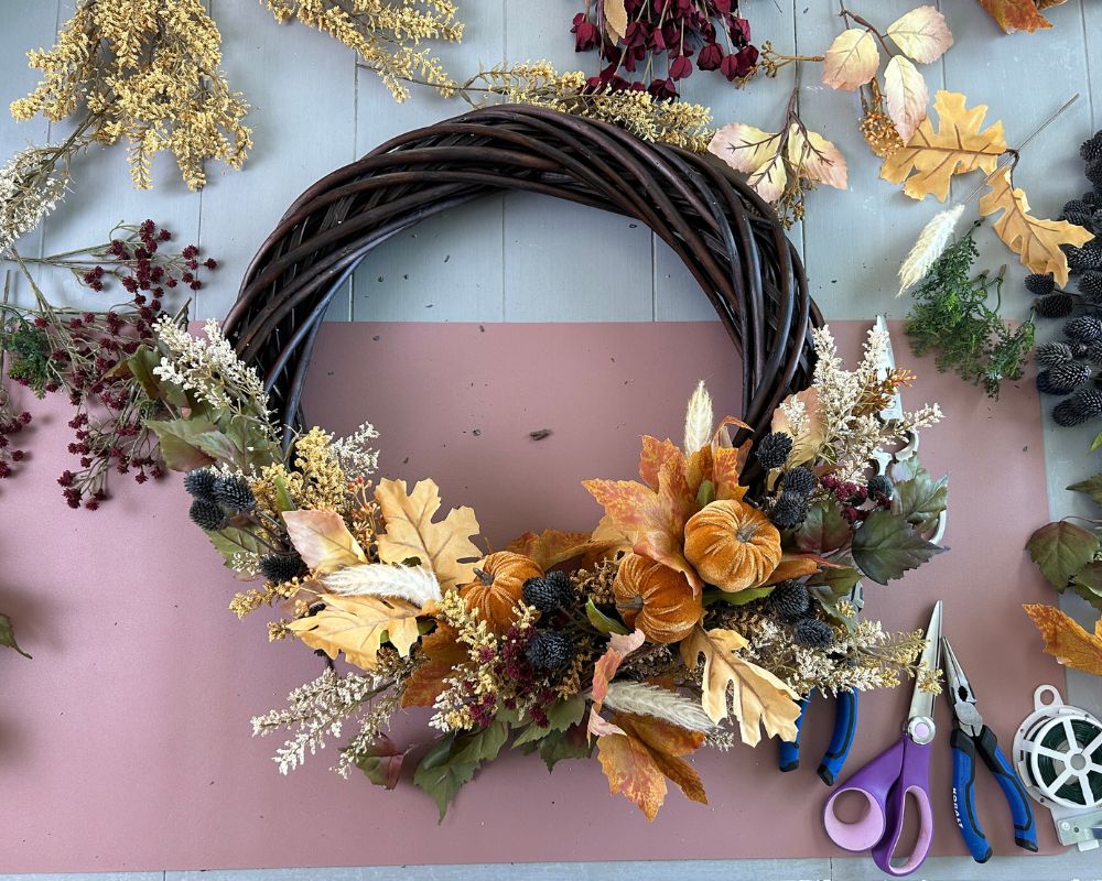 Vine wreath with a mix of floral picks in orange, cream, yellow, burgundy, green and blue.