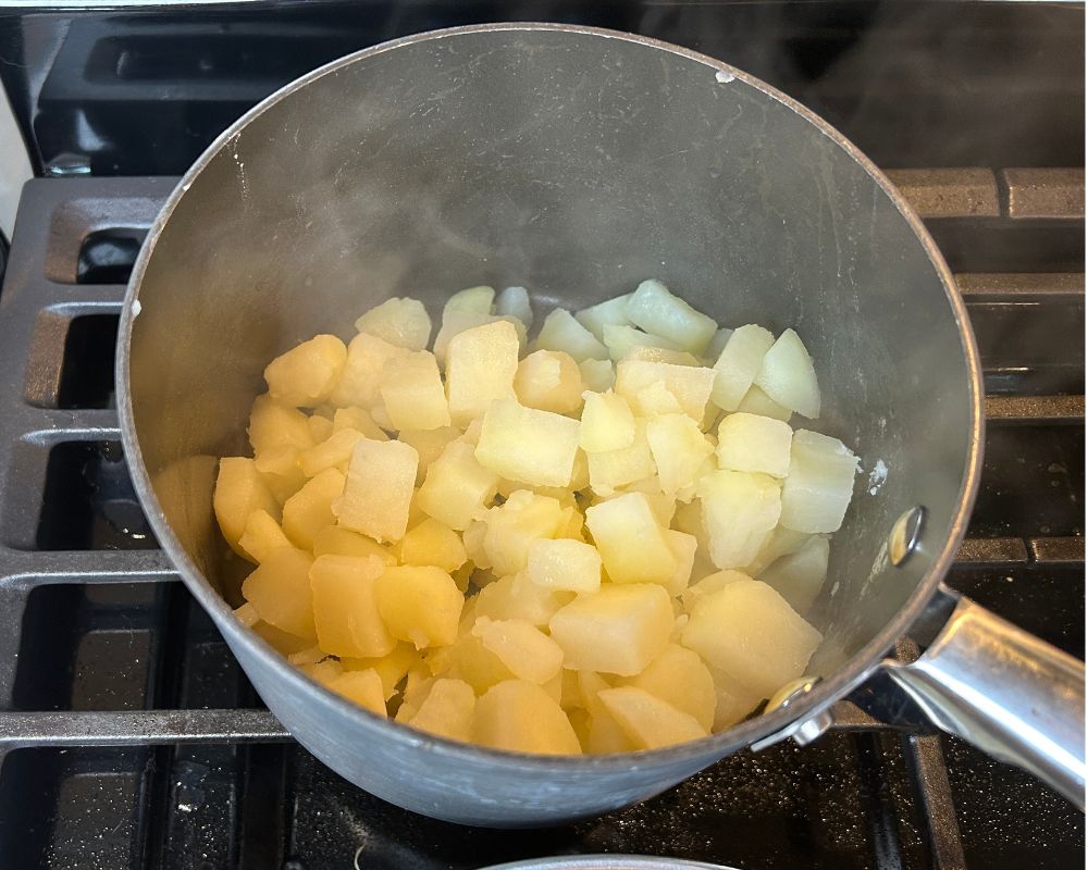 Diced potatoes in a pot on a stove being dried out with heat. 