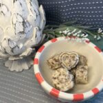 Image of Sweet Pecan Compound butter in heart and pumpkin shapes in a coral and white striped bowl with blue background, white wood artichoke figure and white flowers