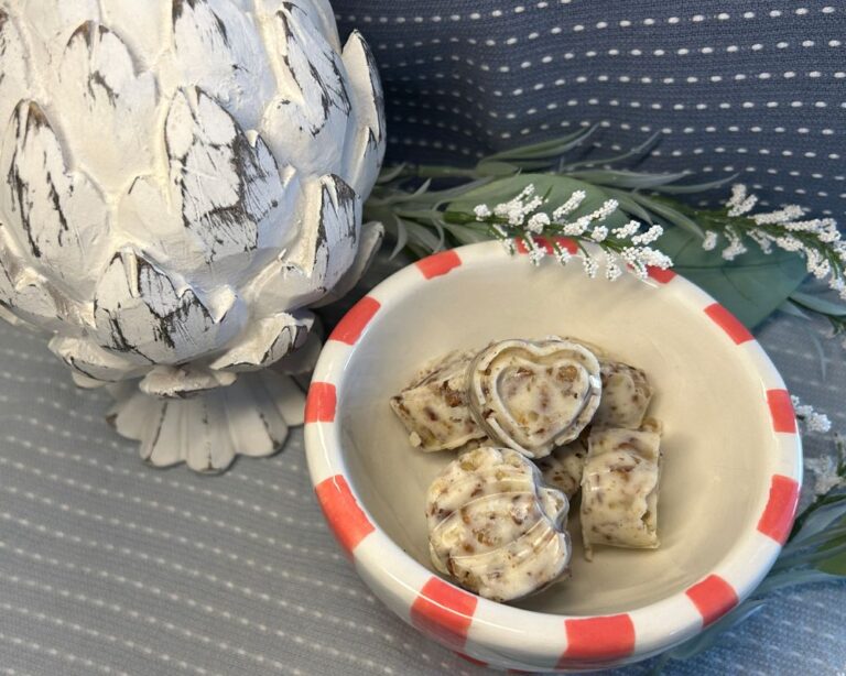 Image of Sweet Pecan Compound butter in heart and pumpkin shapes in a coral and white striped bowl with blue background, white wood artichoke figure and white flowers