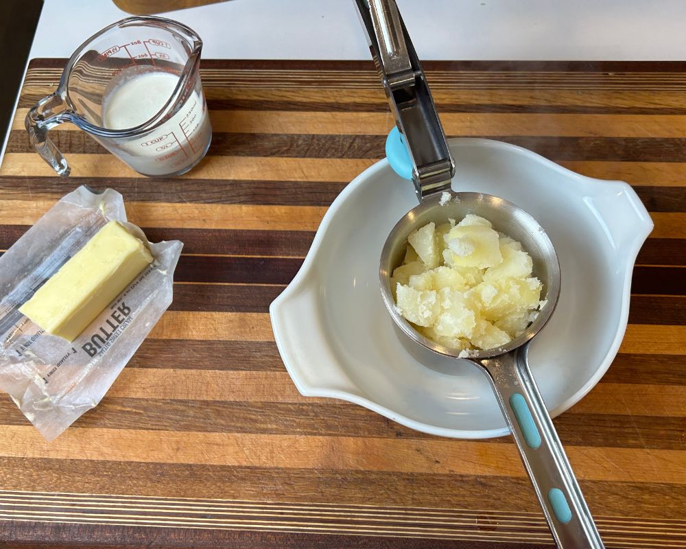 Cooked potatoes in potato ricer basket over serving bowl.