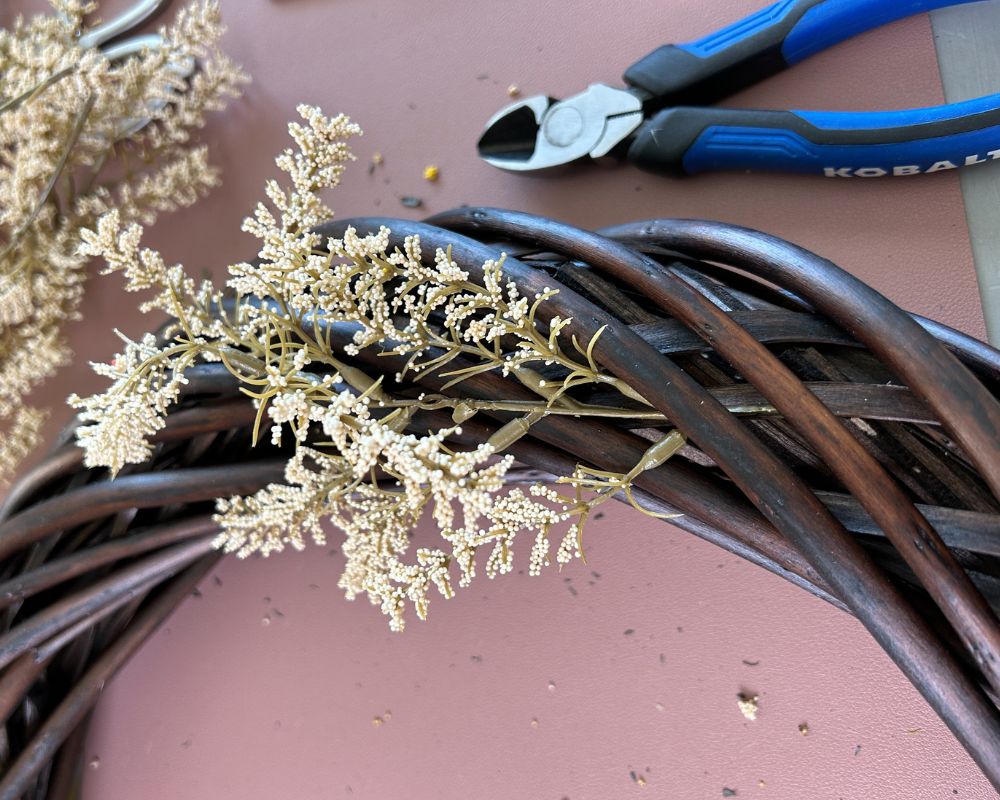 Vine wreath with cream flower pick being attached.