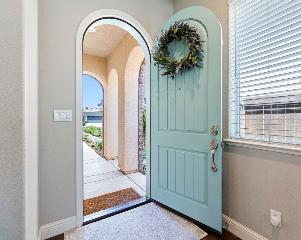 Image of open front robins egg blue door with lavender wreath and small rug.