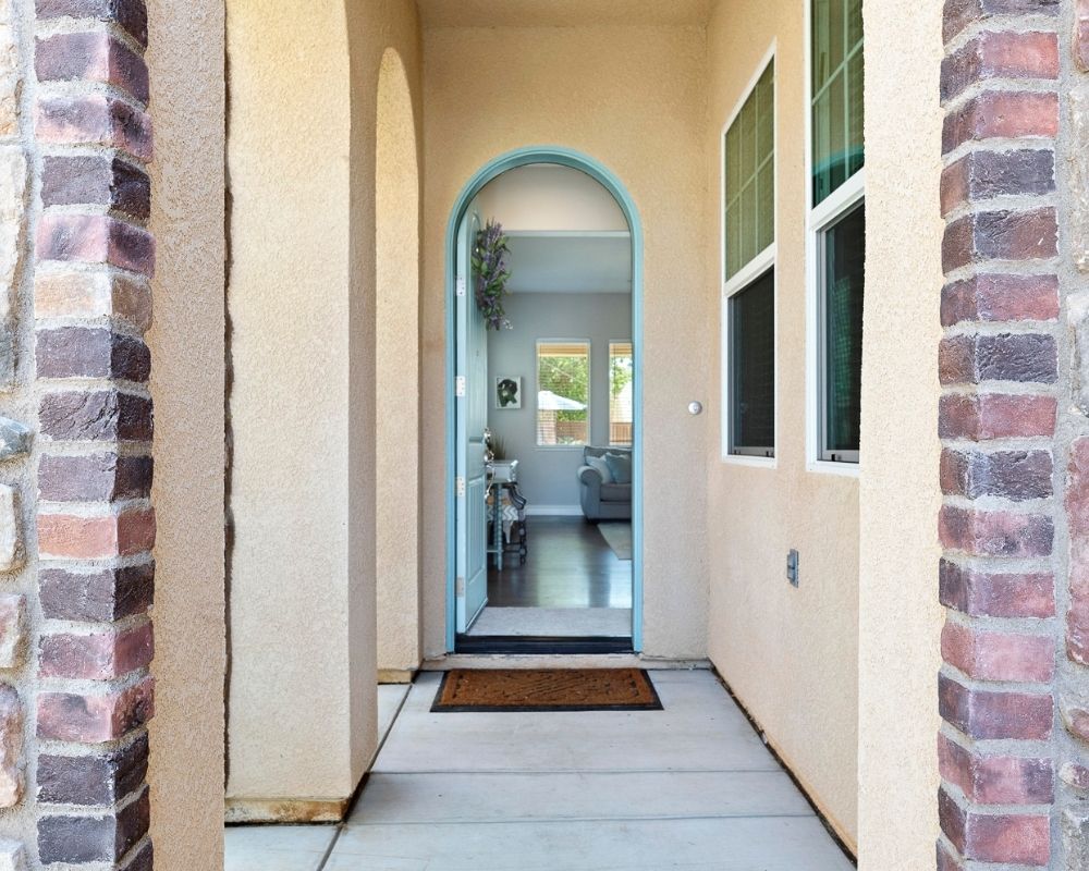 Image of a covered front porch with brick details with a arch top door open and painted robins egg blue.