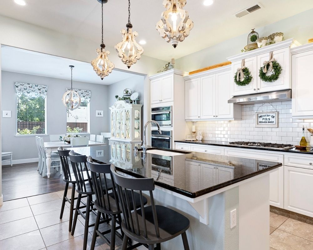 Kitchen with white cabinets, black counters and wood pendant lighting.