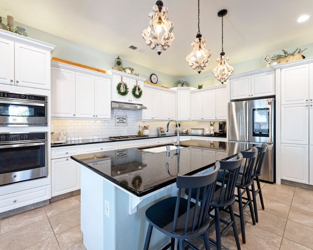 Kitchen with white cabinets, black counters and wood pendant lighting.