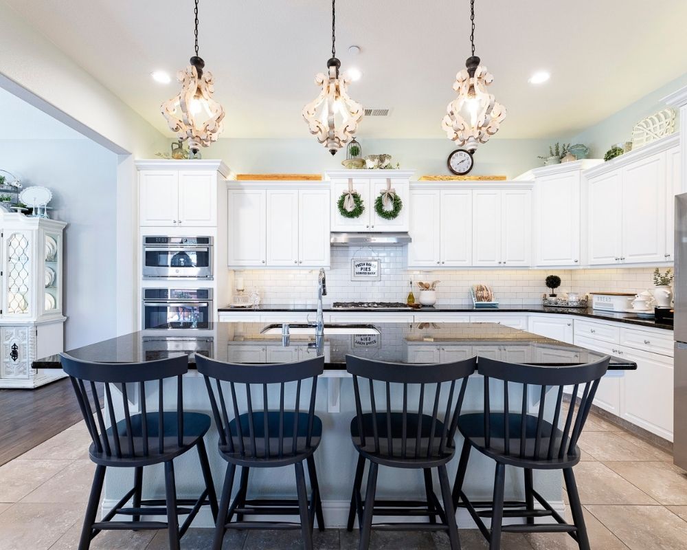 Kitchen with white cabinets, black counters and wood pendant lighting, four counter stools.