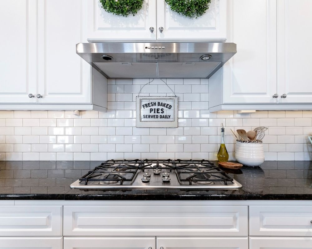 Kitchen with white cabinets, black counters with a stainless stove and hood.