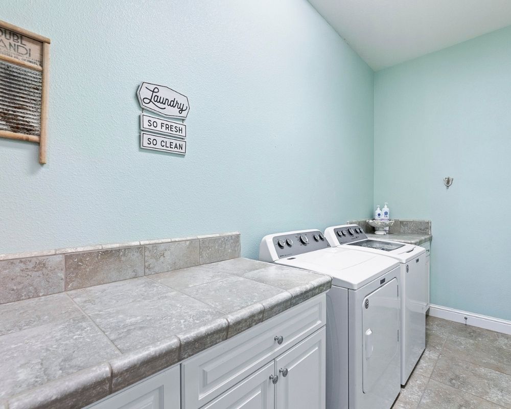 Large laundry room with aqua painted walls, white washer and dryer. White cabinets and tile counter top. 