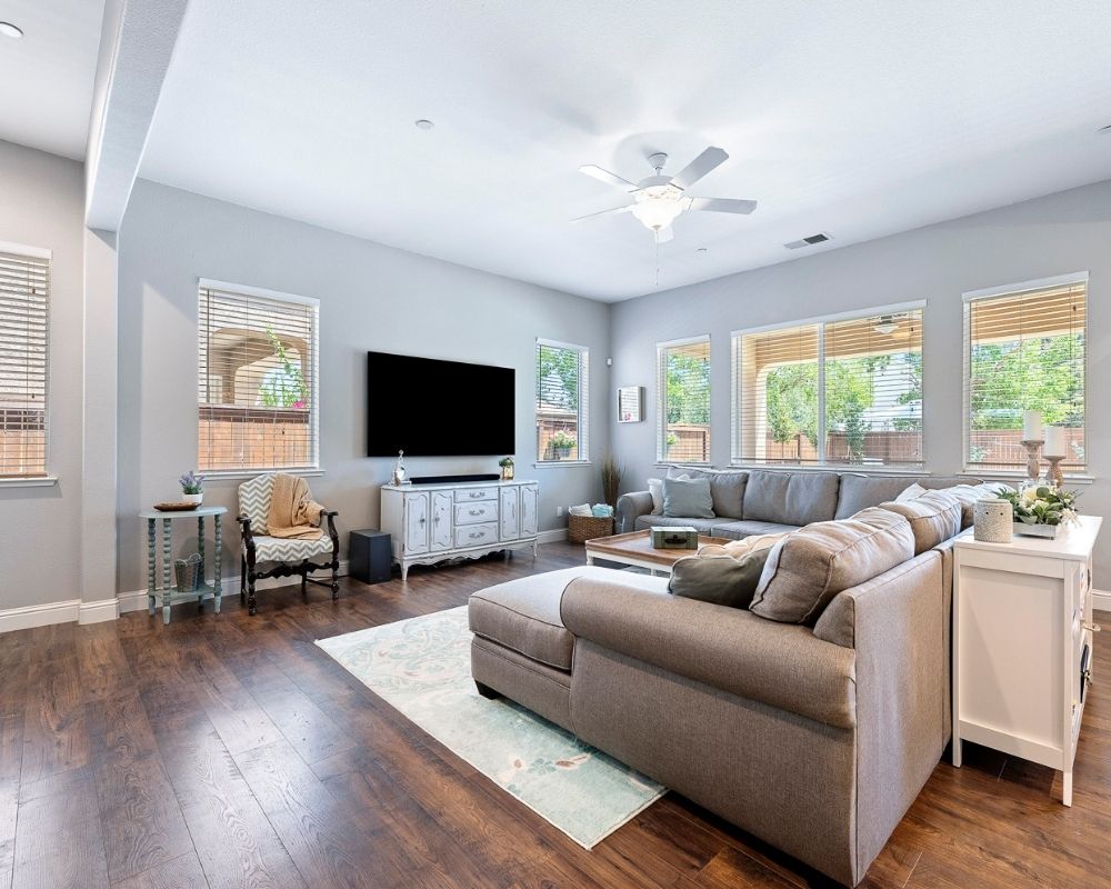 Image of living room with a large gray sectional sofa, blue paisley rug with a tv mounted on the wall over a antique server.