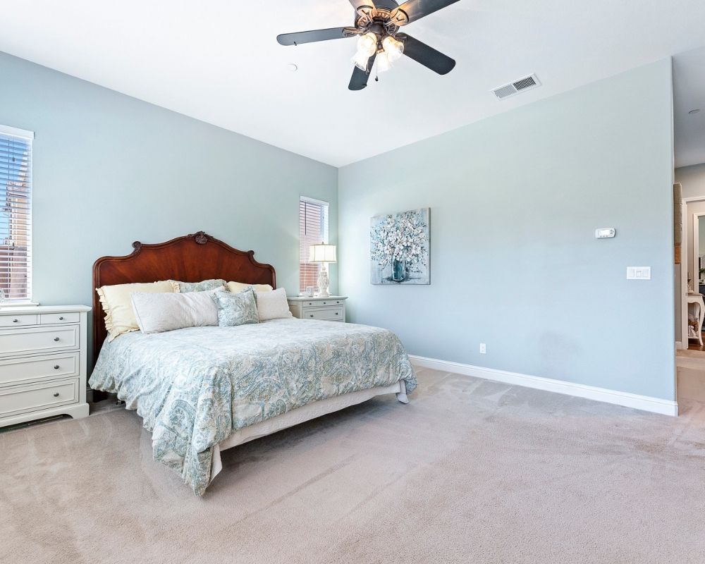 Image of large bedroom with blue walls, a cal king bed with a mahogany headboard and paisley bedding.