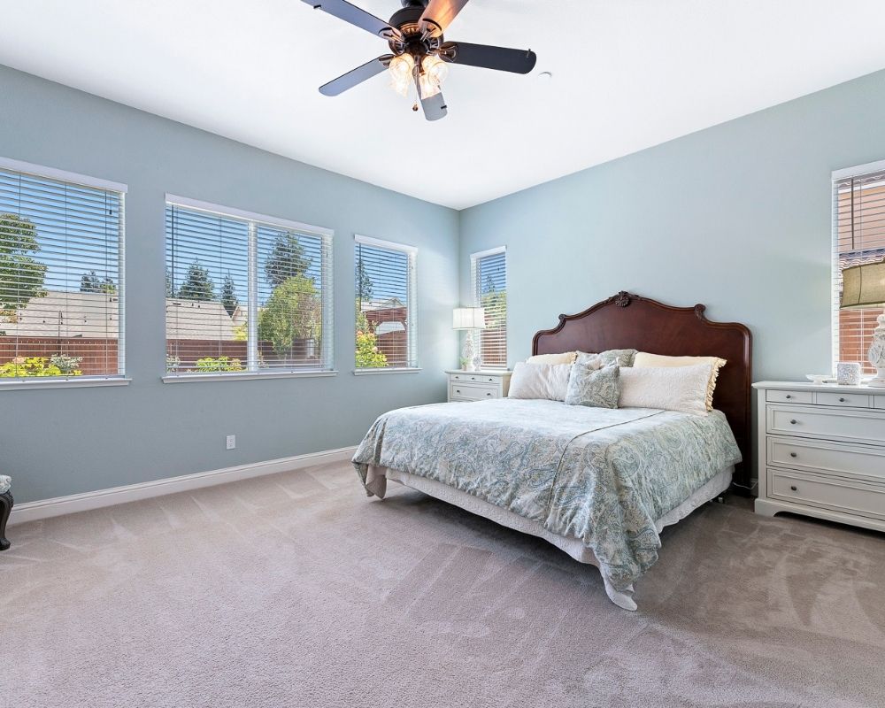 Image of large bedroom with blue walls, a cal king bed with a mahogany headboard and paisley bedding.