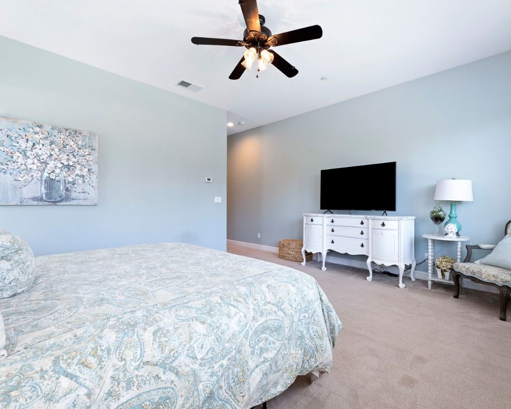 Image of large bedroom with blue walls, a cal king bed with a mahogany headboard and paisley bedding.