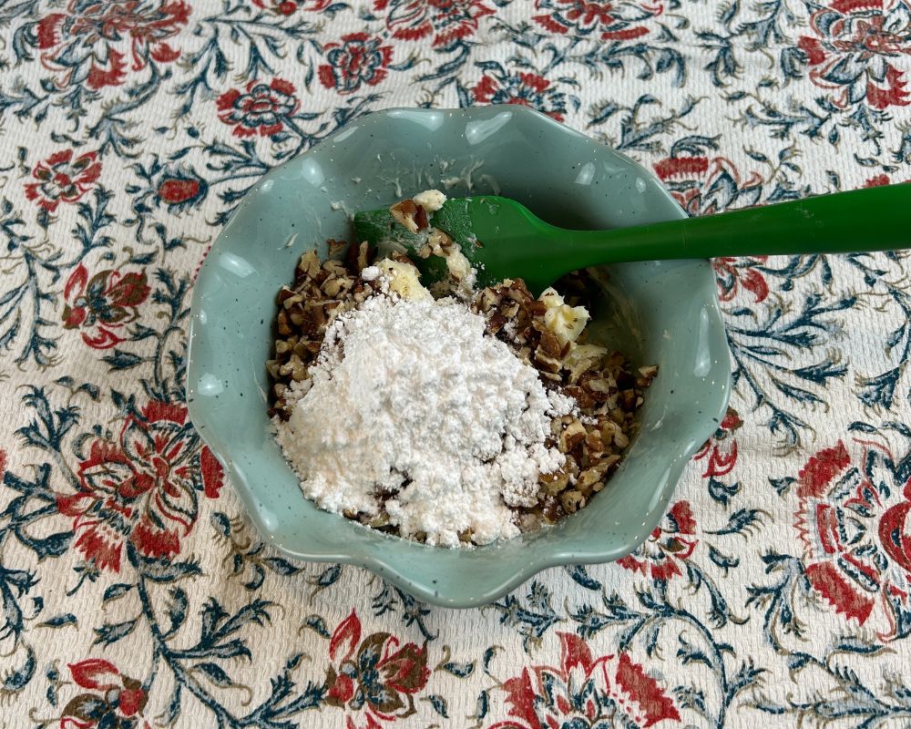 Aqua dish with chopped toasted pecans, softened butter and powdered sugar before mixing.