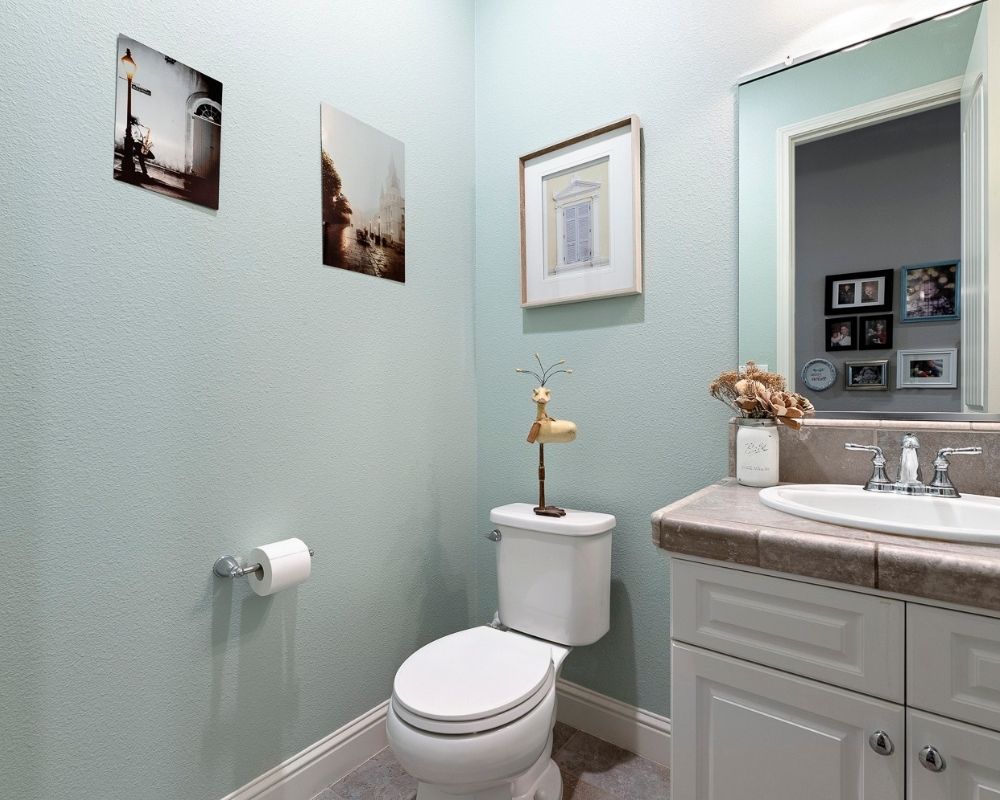 Small powder room with aqua walls, small white sink vanity and art on the walls.