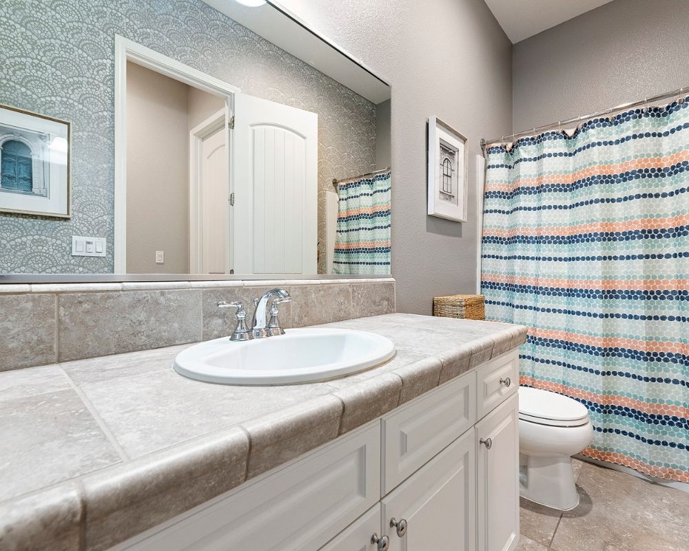 Second bathroom with white cabinets and tile counter sink vanity. Navy, Aqua and Coral shower curtian.