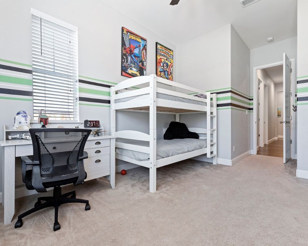 Light gray room with black and green stripes, white bunk bed and white desk.